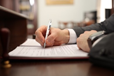 Photo of Notary signing document at table in office, closeup