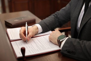 Photo of Notary signing document at wooden table in office, closeup