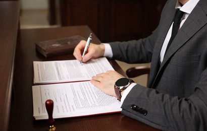 Photo of Notary signing document at wooden table in office, closeup