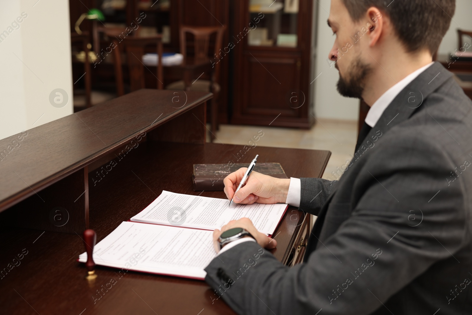 Photo of Notary signing document at wooden table in office