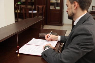 Photo of Notary signing document at wooden table in office