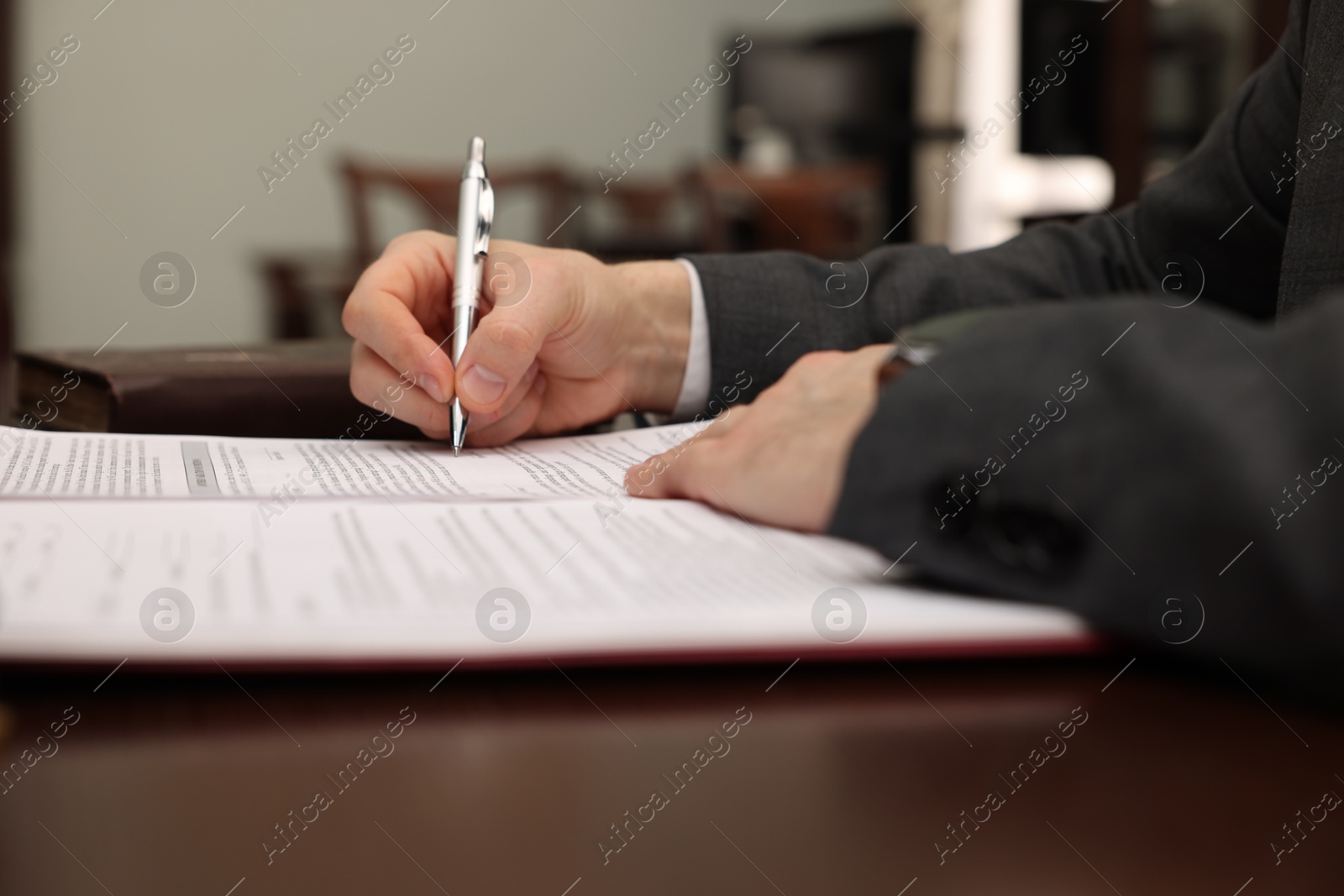 Photo of Notary signing document at table in office, closeup