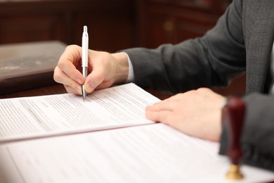 Photo of Notary signing document at table in office, closeup