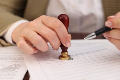 Photo of Notary stamping document at table in office, closeup