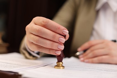 Notary stamping document at table in office, closeup