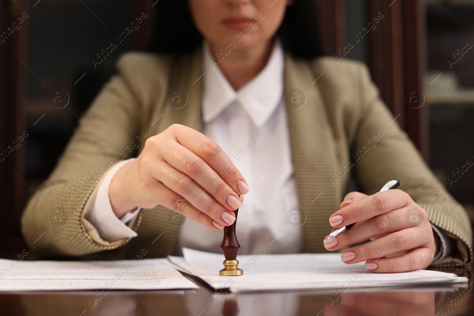 Photo of Notary stamping document at table in office, closeup