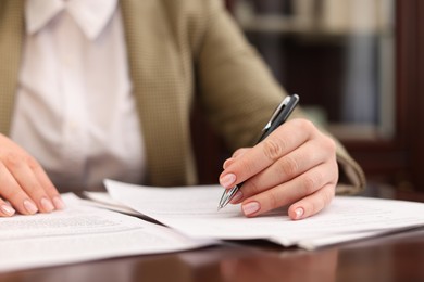 Photo of Notary signing document at table in office, closeup