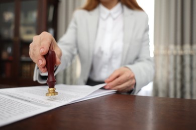 Photo of Notary stamping document at wooden table in office, selective focus