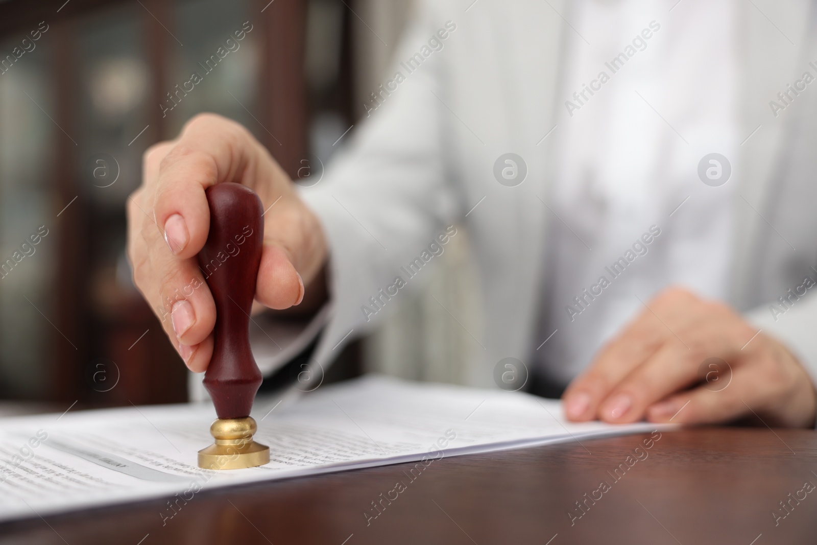 Photo of Notary stamping document at wooden table in office, selective focus