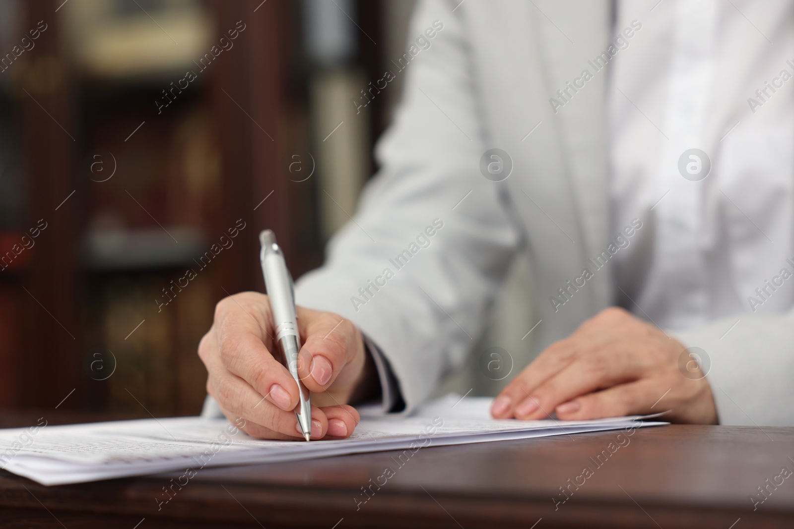 Photo of Notary signing document at table in office, closeup