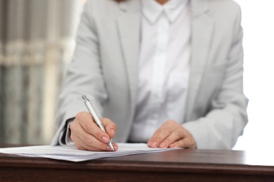 Photo of Notary signing document at table in office, closeup