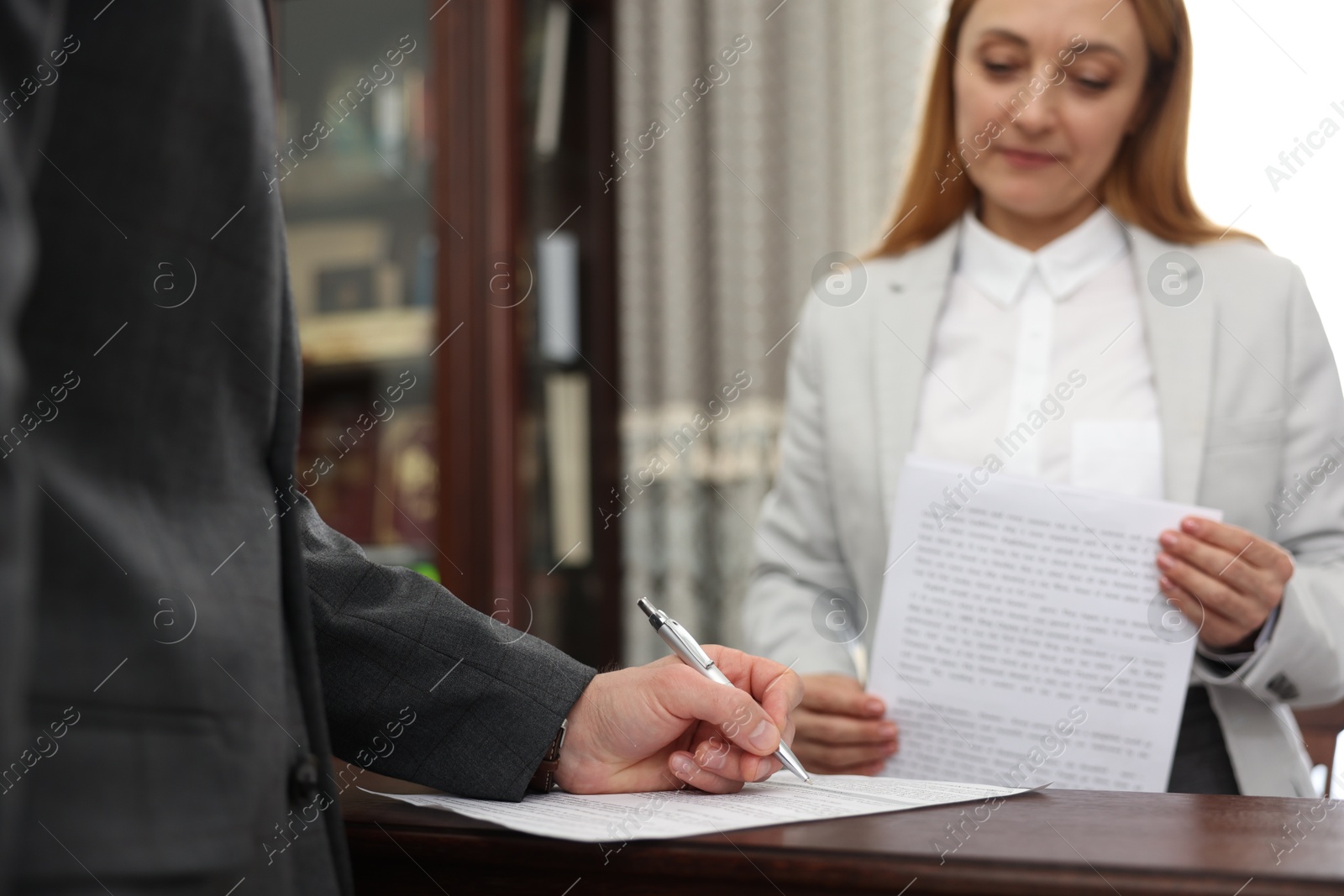 Photo of Notary and client signing document at table in office, closeup