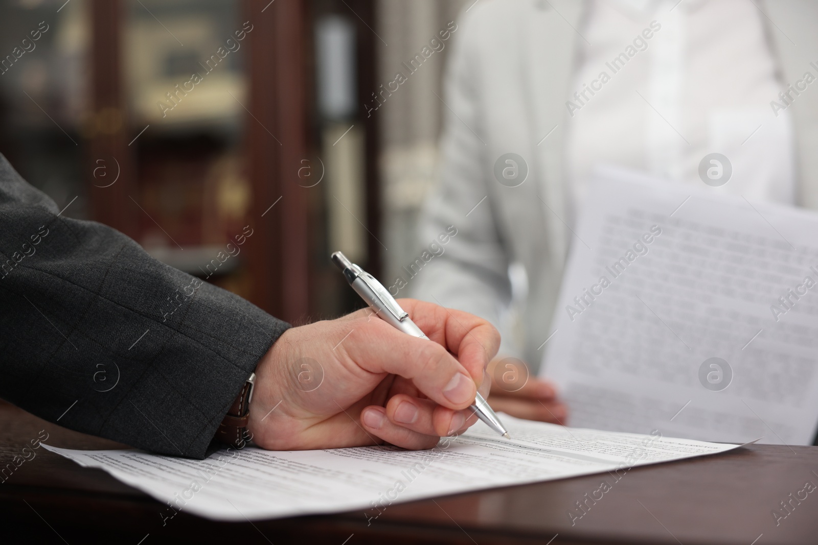 Photo of Notary signing document at wooden table in office, closeup