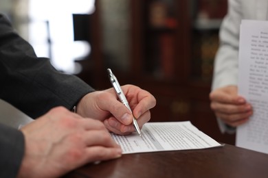 Photo of Notary signing document at wooden table in office, closeup