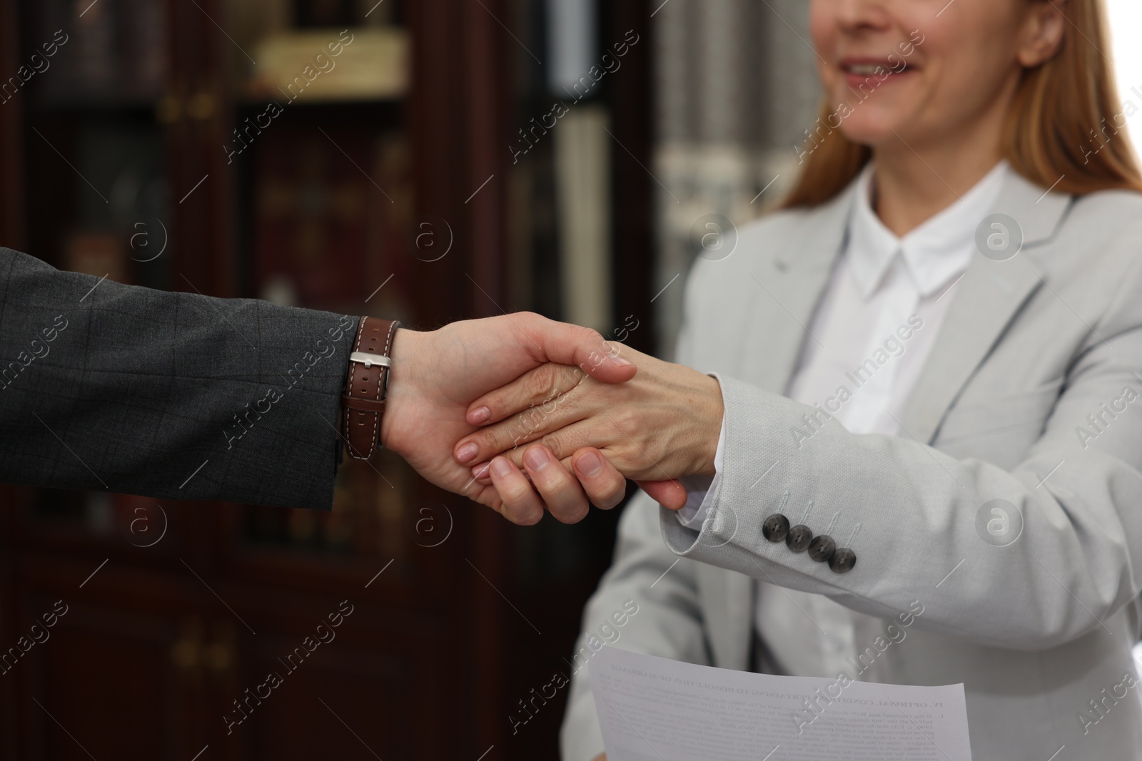 Photo of Smiling notary shaking hands with client in office, closeup