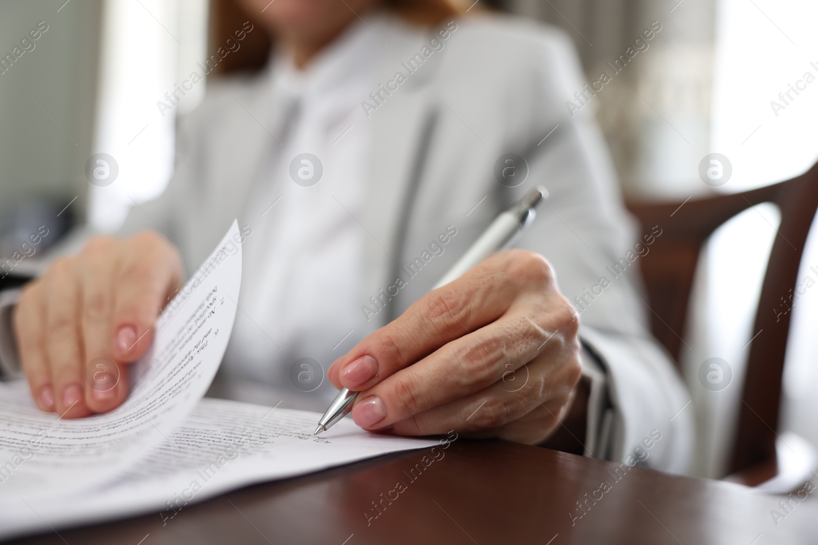 Photo of Notary signing document at table in office, closeup