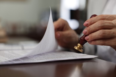 Photo of Notary stamping document at table in office, selective focus