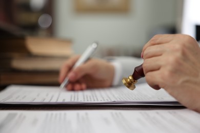 Photo of Notary stamping document at table in office, selective focus