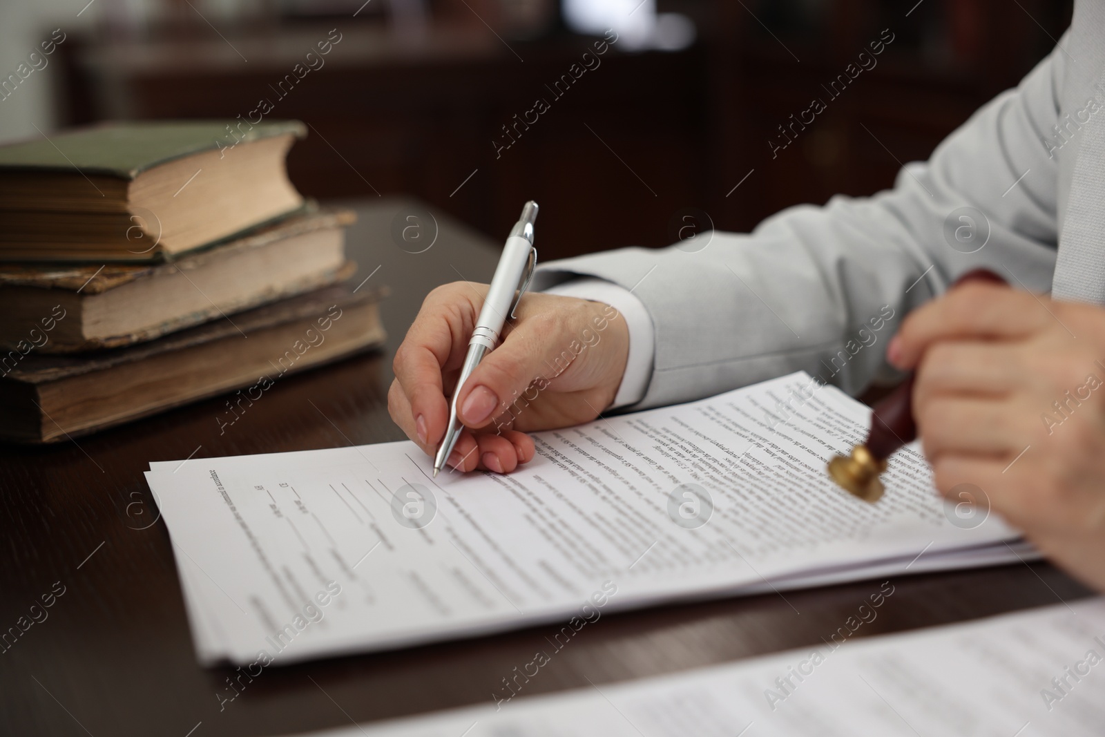 Photo of Notary signing document at table in office, closeup