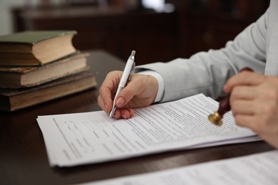 Photo of Notary signing document at table in office, closeup