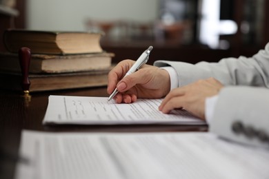 Photo of Notary signing document at table in office, closeup