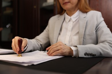 Photo of Notary stamping document at table in office, closeup