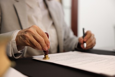 Photo of Notary stamping document at table in office, closeup