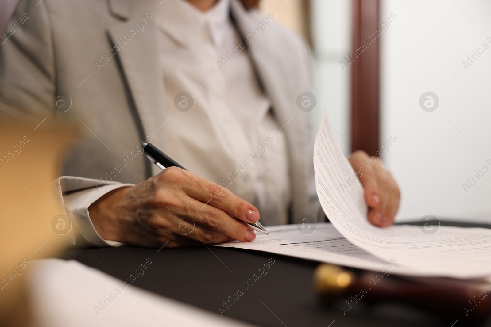 Photo of Notary signing document at table in office, closeup