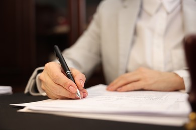 Photo of Notary signing document at table in office, closeup