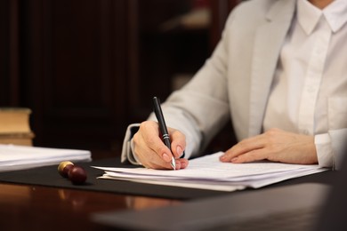 Photo of Notary signing document at table in office, closeup