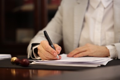 Photo of Notary signing document at table in office, closeup