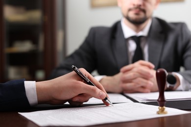 Photo of Notary and client signing document at table in office, selective focus