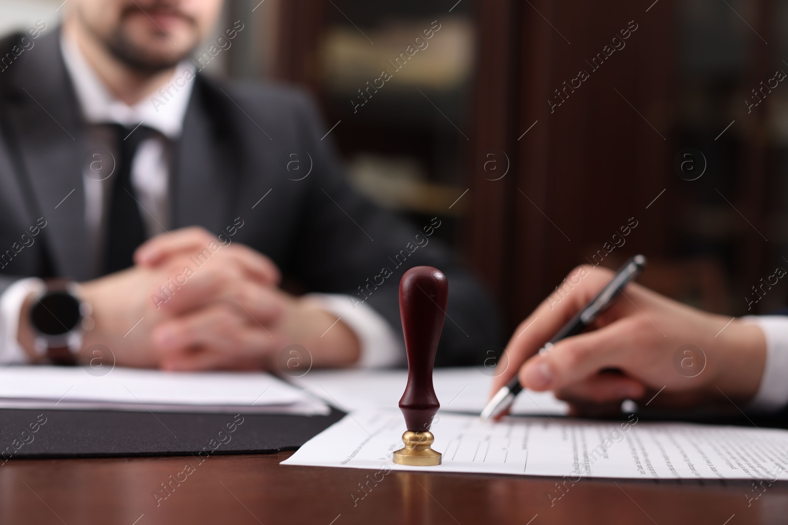 Photo of Notary and client signing document at table in office, selective focus