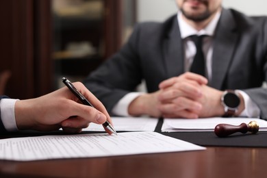 Photo of Notary and client signing document at table in office, selective focus