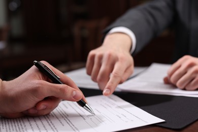 Photo of Notary showing client where to sign document at table in office, closeup