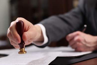 Photo of Notary stamping document at table in office, selective focus