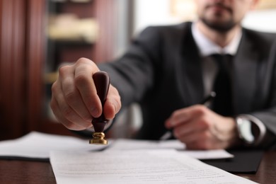 Photo of Notary stamping document at table in office, selective focus