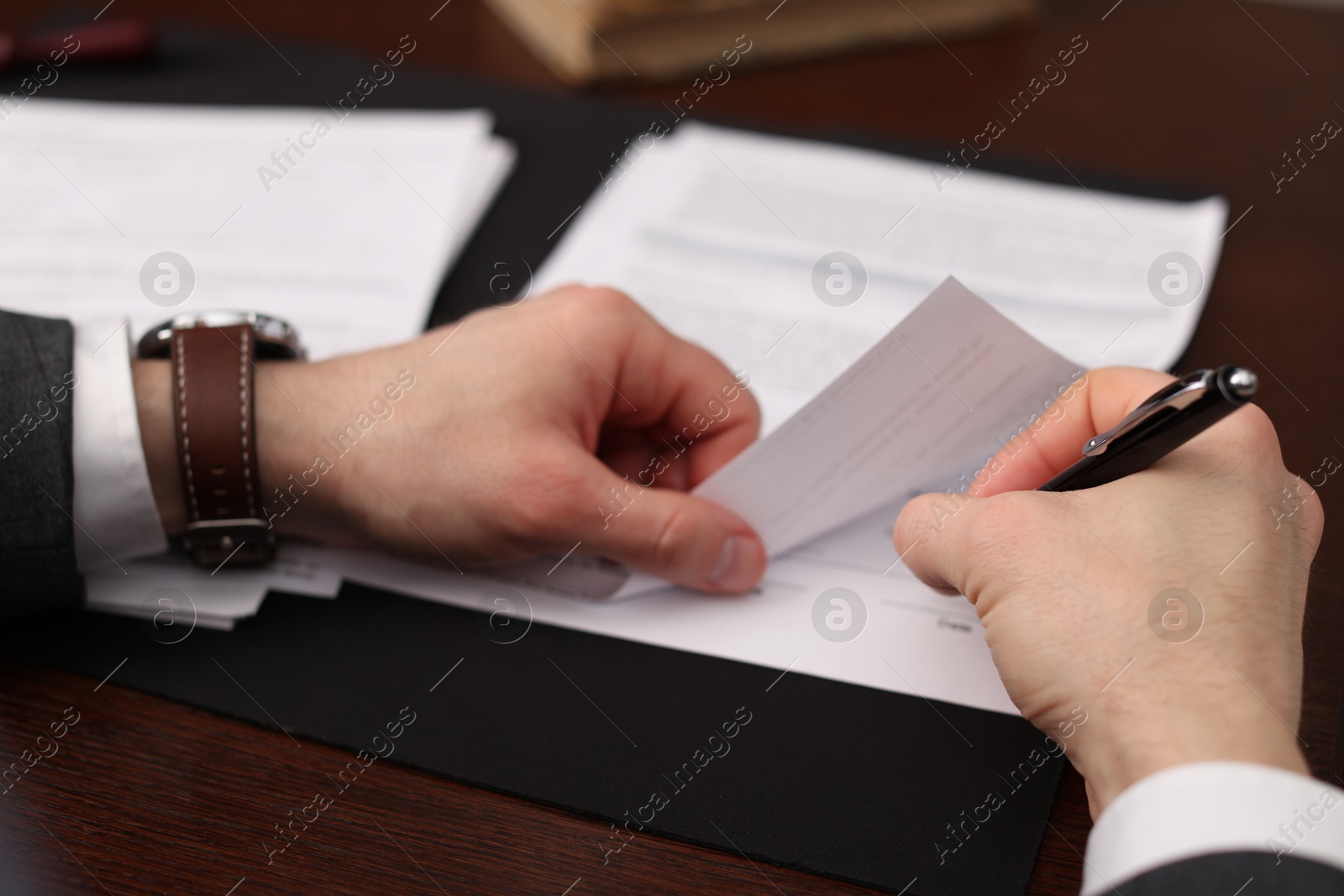 Photo of Notary signing document at wooden table, closeup