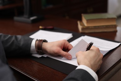 Photo of Notary signing document at wooden table in office, closeup