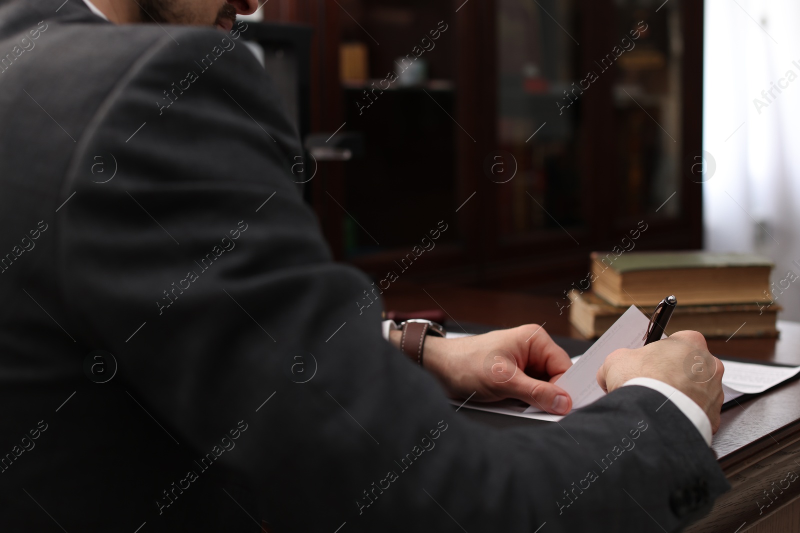 Photo of Notary signing document at wooden table in office, closeup