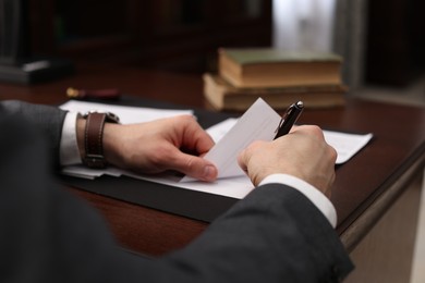 Photo of Notary signing document at wooden table in office, closeup