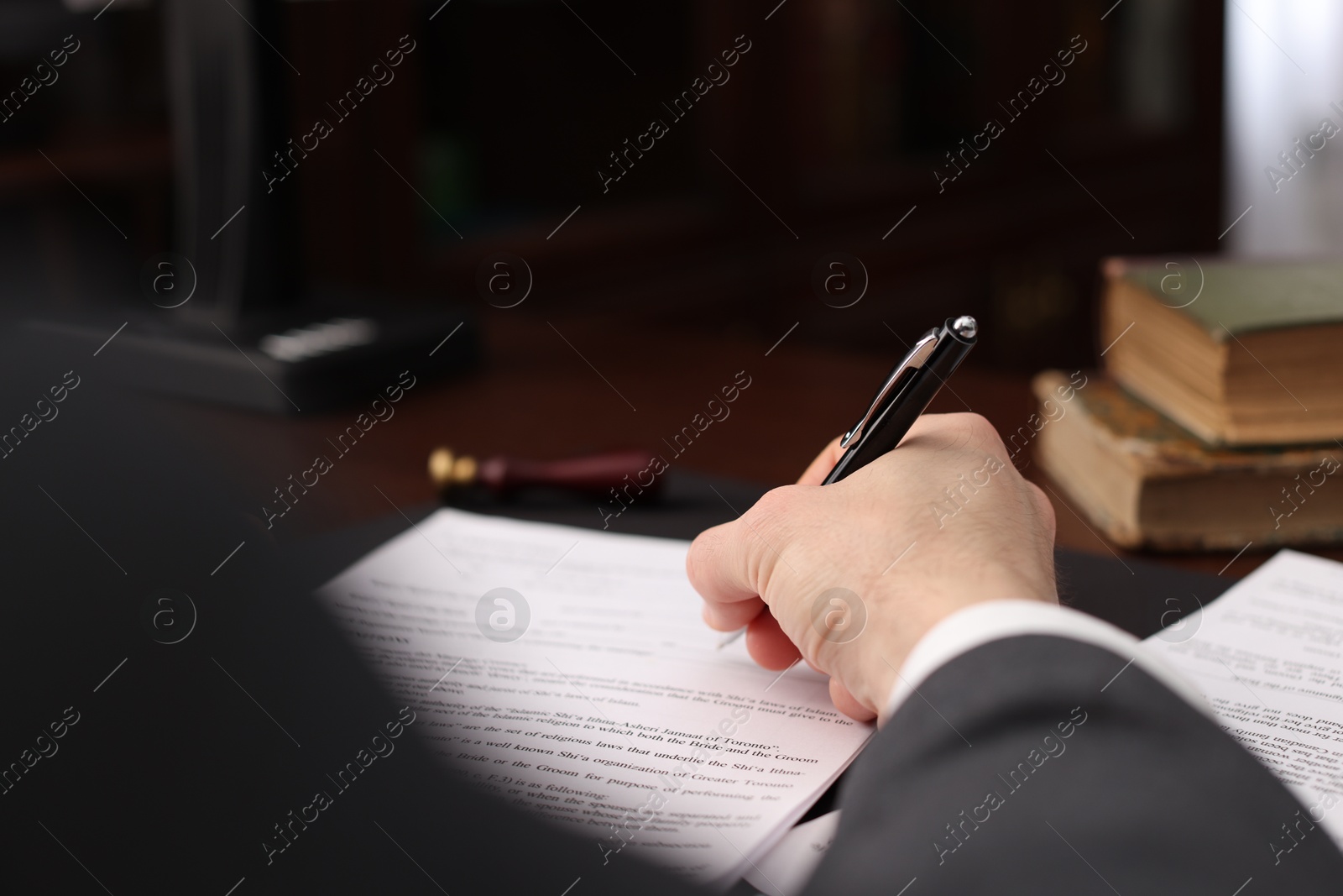 Photo of Notary signing document at table in office, closeup