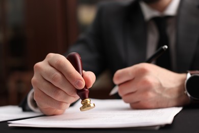 Photo of Notary stamping document at table in office, selective focus