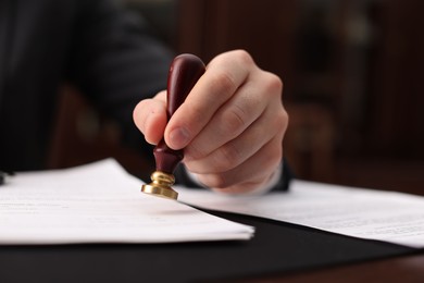 Photo of Notary stamping document at table in office, selective focus