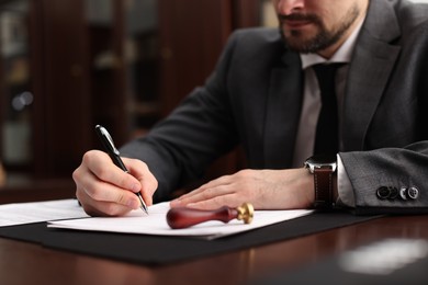 Photo of Notary signing document at table in office, closeup