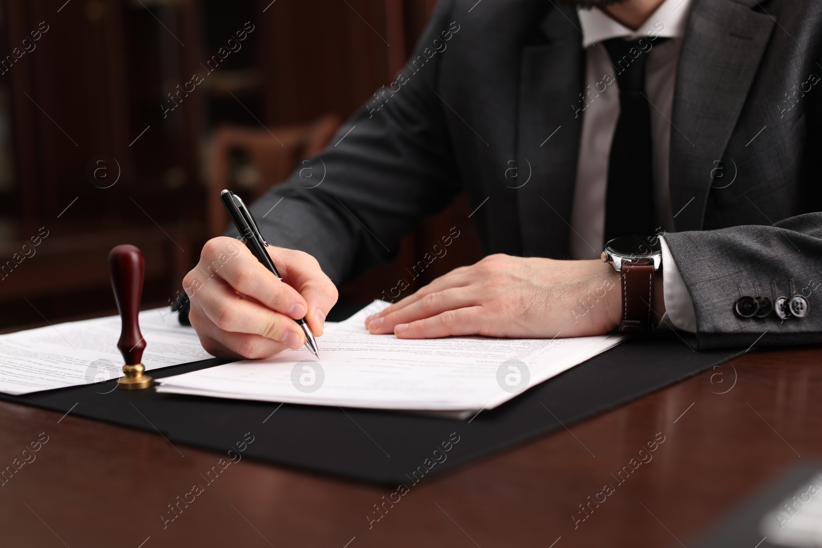 Photo of Notary signing document at table in office, closeup