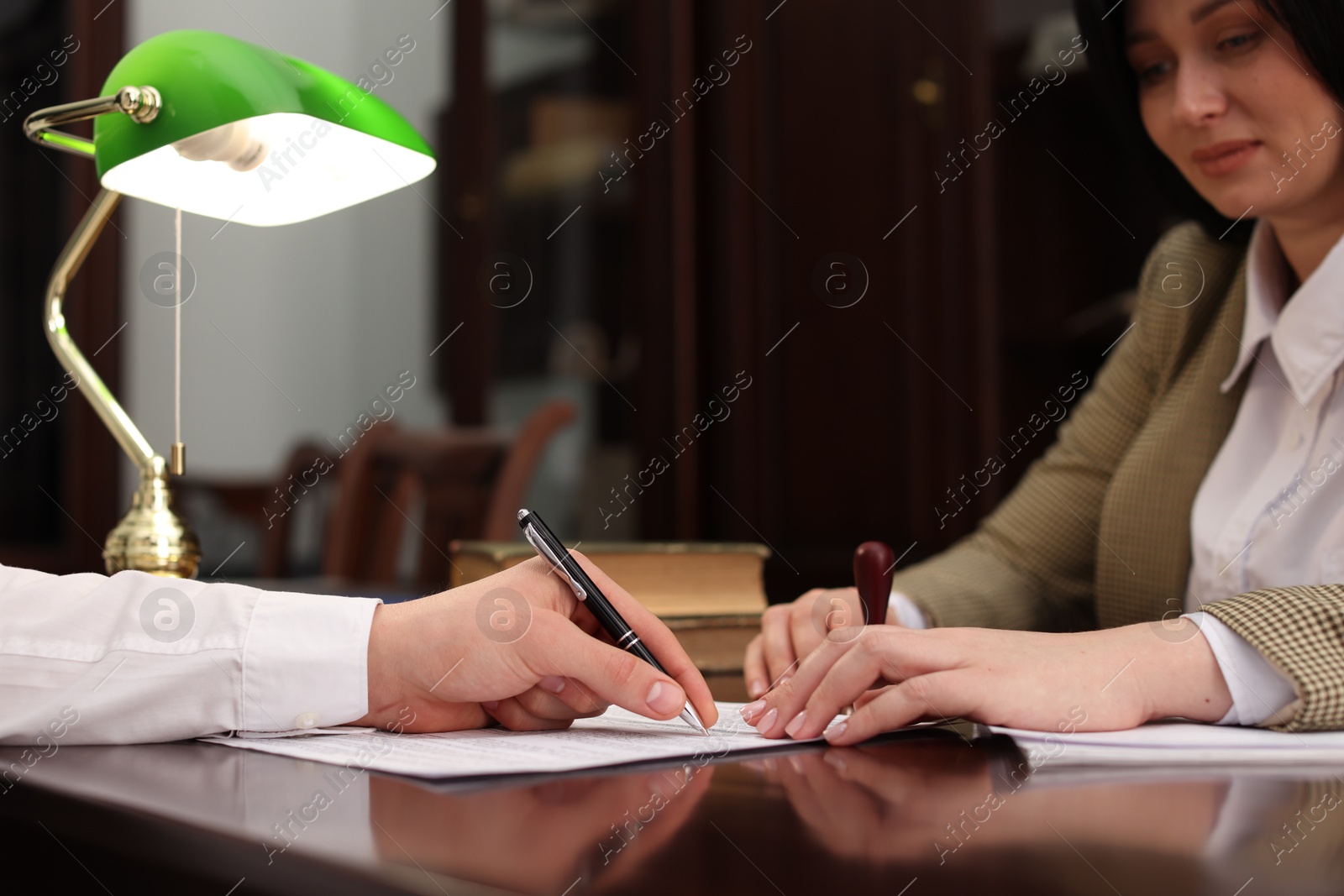 Photo of Notary and client signing document at table in office, closeup