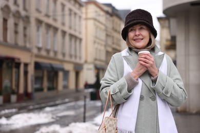 Photo of Smiling senior woman with paper cup on city street. Space for text