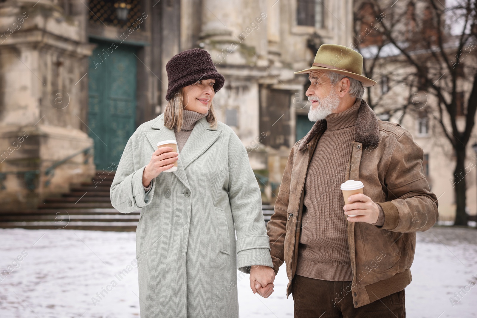 Photo of Happy senior couple with paper cups holding hands on winter day