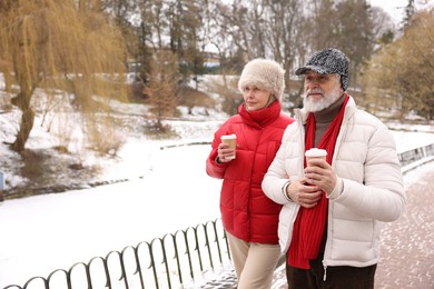 Photo of Lovely senior couple with paper cups walking at winter park. Space for text